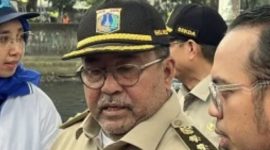 Rano Karno mengenakan baju safari cokelat, mengawasi pengerukan Kali Krukut menggunakan alat berat, sambil memberikan acungan jempol dan tersenyum. (Foto: Istimewa)