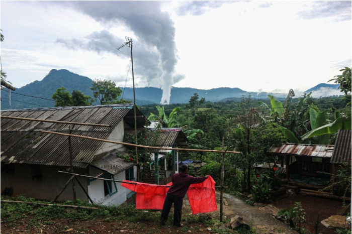 Warga Purwabakti, perbatasan Kabupaten Bogor dan Kabupaten Sukabumi sedang menjemur jas hujan plastik, dengan latar belakang PLTP Gunung Salak.