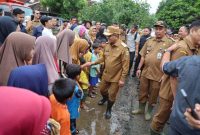 Gubernur Banten, Andra Soni, sedang bersalaman dengan anak-anak dan warga di sebuah jalan tanah yang tampak becek dan berlumpur. (Dok. Biro Adpimpro Banten). 