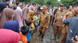 Gubernur Banten, Andra Soni, sedang bersalaman dengan anak-anak dan warga di sebuah jalan tanah yang tampak becek dan berlumpur. (Dok. Biro Adpimpro Banten). 
