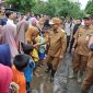 Gubernur Banten, Andra Soni, sedang bersalaman dengan anak-anak dan warga di sebuah jalan tanah yang tampak becek dan berlumpur. (Dok. Biro Adpimpro Banten). 