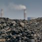 Tumpukan batu bara terlihat di depan cerobong asap sebuah fasilitas industri dengan latar belakang langit biru cerah. (Sumber: Bloomberg – Waldo Swiegers)