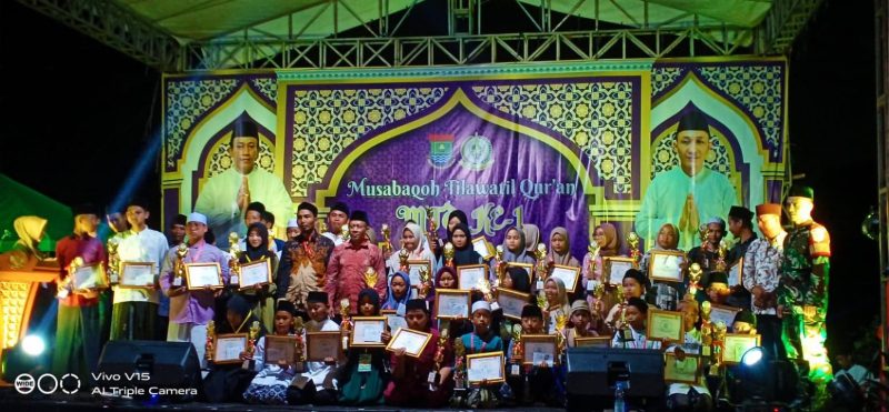 Para pemenang MTQ Ke-1 Desa Kemiri berfoto bersama panitia, tokoh masyarakat, dan unsur Forkopimcam setelah prosesi penyerahan piala dan piagam penghargaan di panggung utama