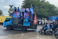 Massa buruh menggelar aksi unjuk rasa dengan mobil komando di ruas jalan Serang, membawa spanduk tuntutan penetapan UMK dan UMSK 2026, di bawah pengawalan aparat keamanan.