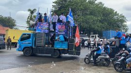 Massa buruh menggelar aksi unjuk rasa dengan mobil komando di ruas jalan Serang, membawa spanduk tuntutan penetapan UMK dan UMSK 2026, di bawah pengawalan aparat keamanan.