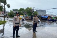 Personel Polsek Pasar Kemis melakukan pemantauan genangan air di Jalan Raya Kutabumi, Kabupaten Tangerang, guna memastikan arus lalu lintas tetap aman saat hujan deras.