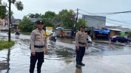 Personel Polsek Pasar Kemis melakukan pemantauan genangan air di Jalan Raya Kutabumi, Kabupaten Tangerang, guna memastikan arus lalu lintas tetap aman saat hujan deras.