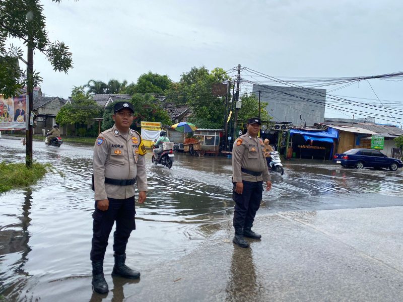 Personel Polsek Pasar Kemis melakukan pemantauan genangan air di Jalan Raya Kutabumi, Kabupaten Tangerang, guna memastikan arus lalu lintas tetap aman saat hujan deras.