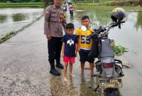 Bhabinkamtibmas Polsek Pasar Kemis memantau genangan air di jalan penghubung Kendal Karet–Sukatani, memastikan akses warga tetap aman dilalui meski hujan deras.