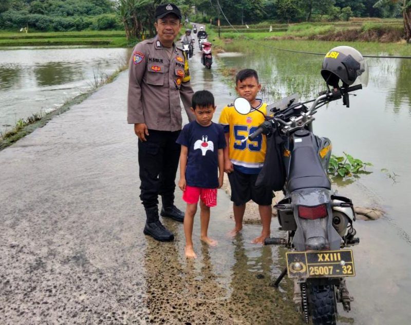 Bhabinkamtibmas Polsek Pasar Kemis memantau genangan air di jalan penghubung Kendal Karet–Sukatani, memastikan akses warga tetap aman dilalui meski hujan deras.