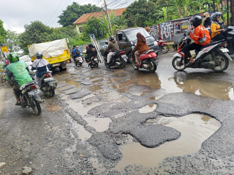 Jalan Raya Pasar Kemis rusak parah dan dipenuhi lubang besar yang tergenang air. Pengendara motor harus ekstra hati-hati saat melintas karena licin dan rawan kecelakaan.