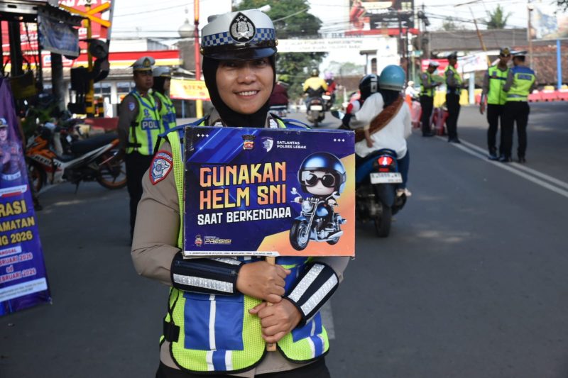Polwan Satlantas Polres Lebak menunjukkan poster imbauan penggunaan helm SNI kepada pengendara saat Operasi Keselamatan Maung 2026.