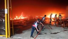 Petugas pemadam kebakaran berupaya memadamkan api yang melalap area gudang, dengan kobaran api masih terlihat cukup besar di latar belakang.