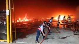 Petugas pemadam kebakaran berupaya memadamkan api yang melalap area gudang, dengan kobaran api masih terlihat cukup besar di latar belakang.