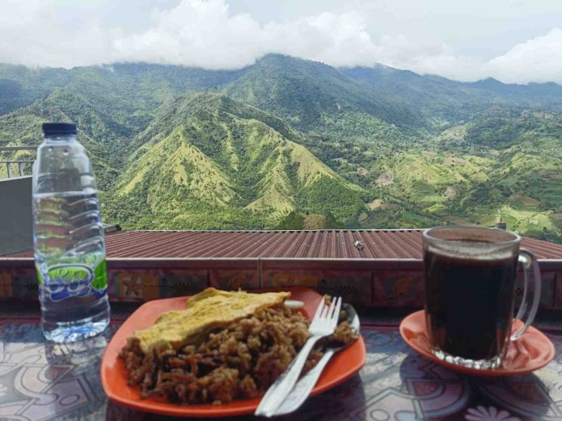 Wisatawan menikmati kopi hangat dan kuliner lokal dengan latar panorama pegunungan hijau di Enrekang, Sulawesi Selatan.
