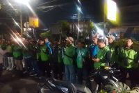 Petugas kepolisian memberikan arahan kepada rombongan pengemudi ojek online sebelum keberangkatan pengawalan menuju Monas pada malam hari.