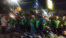 Petugas kepolisian memberikan arahan kepada rombongan pengemudi ojek online sebelum keberangkatan pengawalan menuju Monas pada malam hari.