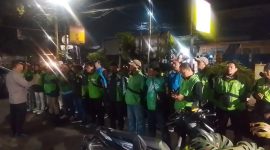 Petugas kepolisian memberikan arahan kepada rombongan pengemudi ojek online sebelum keberangkatan pengawalan menuju Monas pada malam hari.