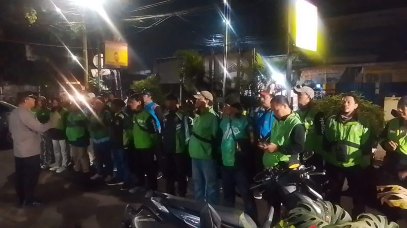 Petugas kepolisian memberikan arahan kepada rombongan pengemudi ojek online sebelum keberangkatan pengawalan menuju Monas pada malam hari.
