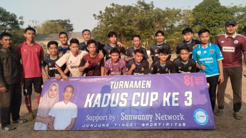 Para pemain turnamen sepak bola berfoto bersama di belakang banner bertuliskan "TURNAMEN KADUS CUP KE 3" dalam rangka perayaan HUT RI ke-81 di Desa Kemiri.